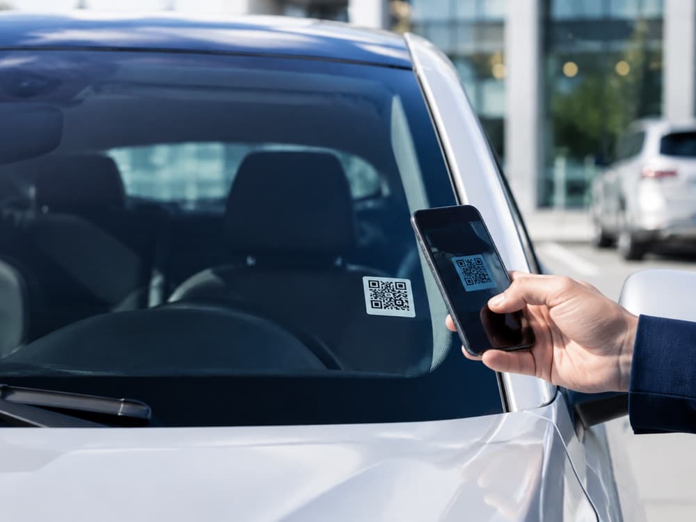 Araç ön camına yapıştırılmış QR sticker'ı telefonuyla okutan kişi